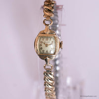 Vintage gold watch with a decorative band on a light pink background