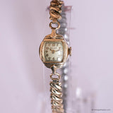 Vintage gold watch with a decorative band on a light pink background