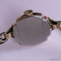 Back view of a gold watch with visible branding and model number on a white background