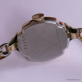 Back view of a gold watch with visible branding and model number on a white background